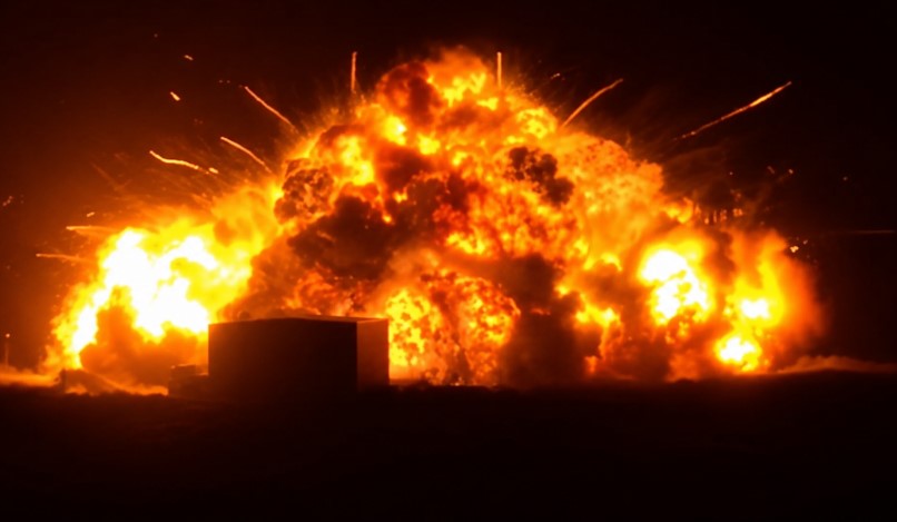Massive nighttime explosion during a rocket test at a launch facility, with intense fireball and smoke illuminating the dark sky.