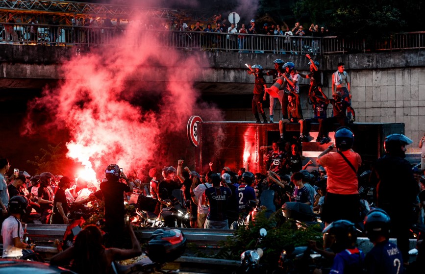 PSG supporters gather amid red flare smoke and heavy crowds during post-Champions League celebrations in Paris, as police monitor unrest following Paris Saint-Germain's historic European triumph.